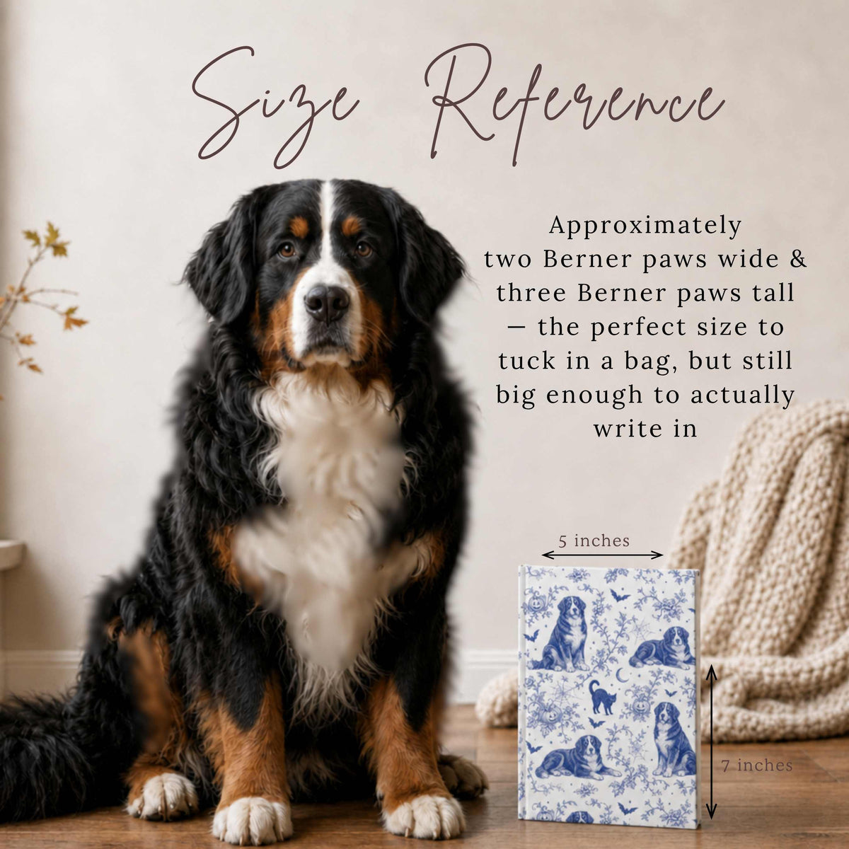 A seated adult Bernese Mountain Dog beside a hardcover journal featuring vintage blue toile linework with Bernese Mountain Dogs among bats, pumpkins, and a black cat on white, with dimension arrows labeled 5 inches and 7 inches, on a wood floor with a knit blanket nearby. Text reads "Size Reference: Approximately two Berner paws wide and three Berner paws tall.”