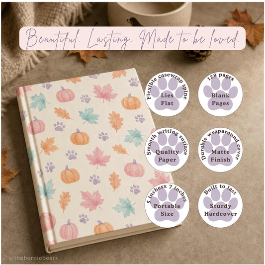 A hardcover journal featuring soft pastel pumpkins, leaves, and paw prints on cream, resting on a warm taupe surface beside a small dog bowl and a pinecone. Text reads "Beautiful. Lasting. Made to be loved." with six paw-print badges: Lies Flat, Blank Pages, Quality Paper, Matte Finish, Portable Size, and Sturdy Hardcover.