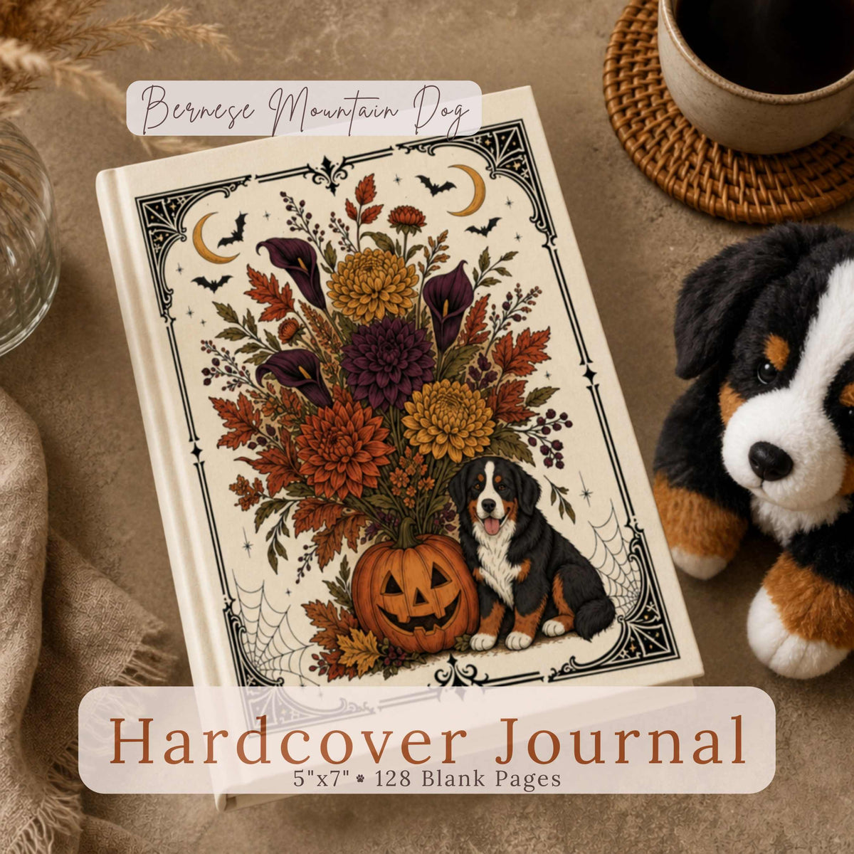 A Bernese Mountain Dog plush toy sits beside a hardcover journal featuring a Bernese Mountain Dog puppy beside an ornate jack-o-lantern floral bouquet framed in vintage Halloween detail on cream, with a circular close-up inset of the pattern, on a warm taupe surface with dried pampas grass and a coffee cup. Text reads "Bernese Mountain Dog Hardcover Journal, 5"x7" • 128 Blank Pages."