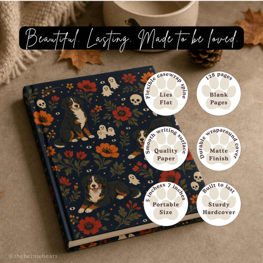 A hardcover journal featuring playful Bernese Mountain Dogs among bold red and orange florals with friendly ghosts, skulls, and watchful eyes on midnight navy, resting on a warm taupe surface beside a small dog bowl and a pinecone. Text reads "Beautiful. Lasting. Made to be loved." with six paw-print badges: Lies Flat, Blank Pages, Quality Paper, Matte Finish, Portable Size, and Sturdy Hardcover.